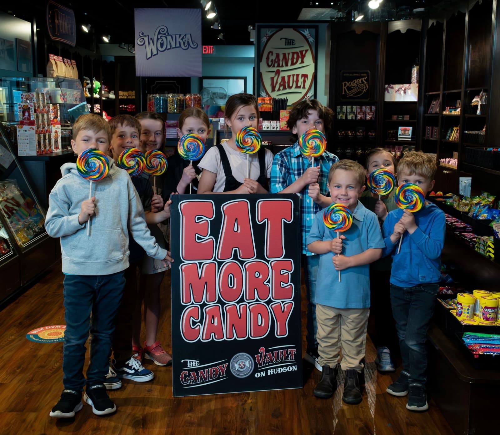 Kids with Whirly Pops by the Eat More Candy sign inside The Candy Vault
